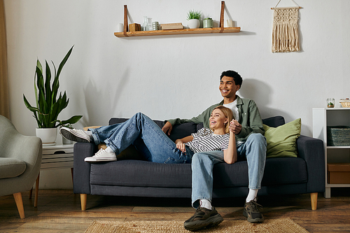 A young multicultural couple relaxes and enjoys each others company on a comfortable sofa in their modern apartment.