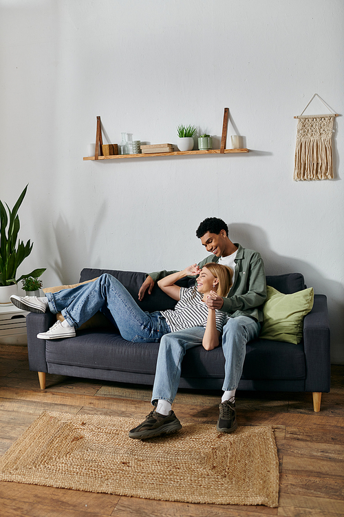 A young, multicultural couple relax and enjoy each others company on a comfortable sofa in their modern apartment.