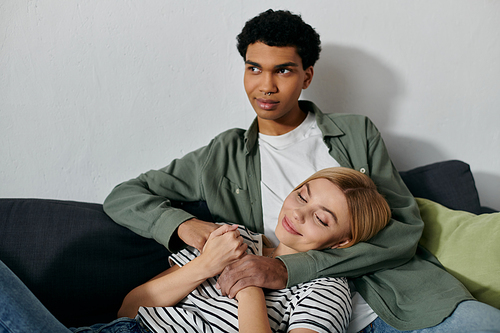 A young, multicultural couple relaxes together on a couch in their modern apartment.