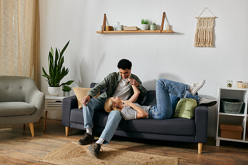 A young interracial couple enjoys a moment of intimacy on a couch in their modern apartment.