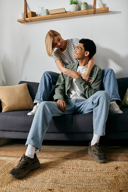 A young couple, a man and a woman, cuddle on a sofa in a modern apartment.