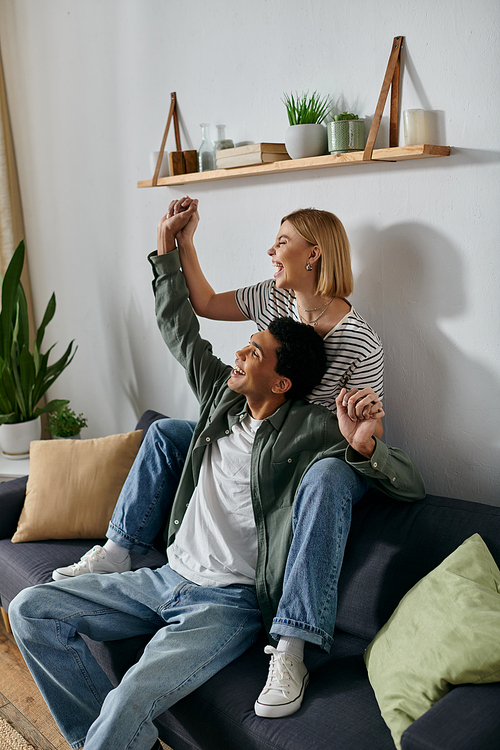 A young, multicultural couple celebrates in their modern apartment, filled with laughter and happiness.