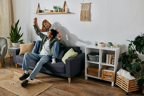 A young, multicultural couple enjoys a playful moment on a couch in their modern apartment.