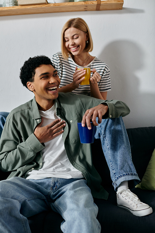 A young multicultural couple relaxes on a couch in a modern apartment, sharing a laugh and enjoying their afternoon together.