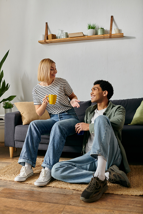 A young, multicultural couple relaxes in their apartment, sharing a cozy moment and a warm drink.