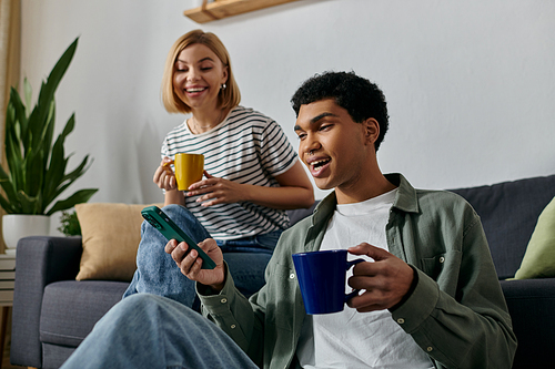 A young multicultural couple enjoys a relaxed afternoon in their modern apartment, sharing laughter and a cup of coffee.