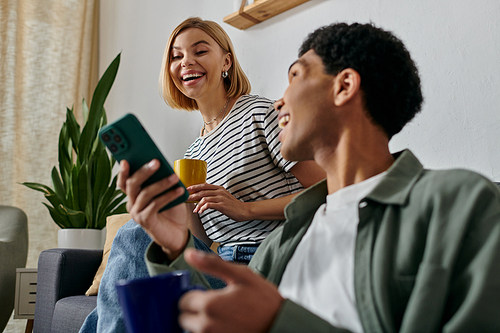 A young interracial couple enjoys a moment of laughter and connection while relaxing in their modern apartment.