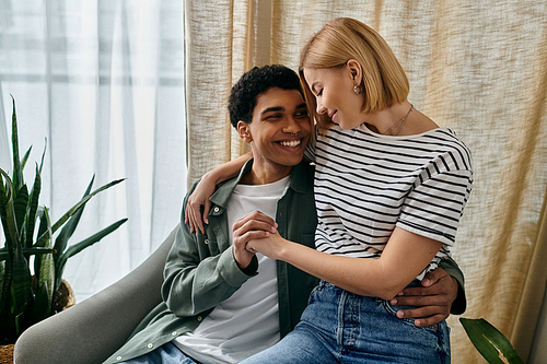 A young multicultural couple enjoys a cozy moment together in a modern apartment, with natural light streaming in through the window.