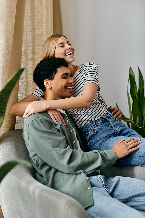 A young multicultural couple sits on a couch in a modern apartment, laughing and enjoying each others company.