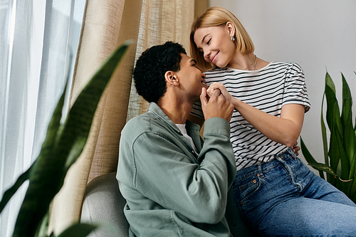 A young multicultural couple shares a tender moment in their modern apartment, with natural light streaming in through the window.