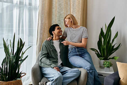 A young interracial couple enjoys a moment of intimacy and laughter in their modern apartment, bathed in natural light.