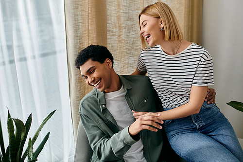 A young multicultural couple shares a moment of laughter together in their modern apartment.