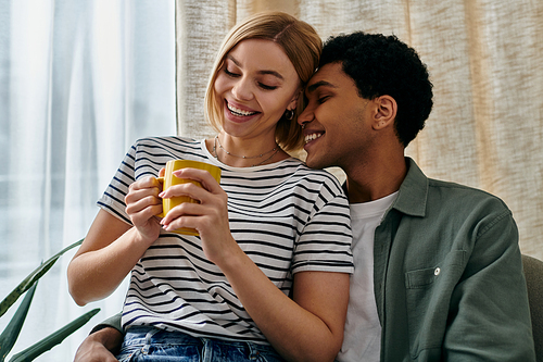 A young, multicultural couple shares a warm moment in their modern apartment, enjoying a cup of coffee together.