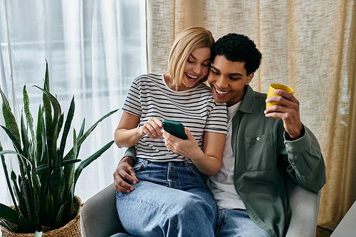 A young couple, one with a phone and the other with a drink, laughs together in a modern apartment.