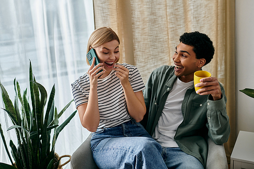 Young couple in modern apartment: woman smiles on phone call, man laughs with coffee.