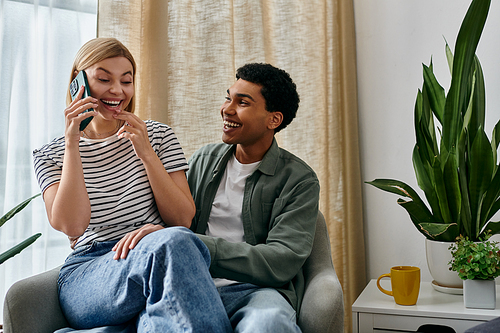 A young couple, laughing and enjoying each others company, sits in a modern apartment with a plant in the background.