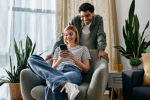 A young couple, relaxes in a modern apartment, the woman scrolling on her phone while her man looks on.