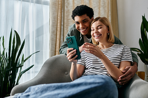 A young couple shares a laugh while looking at a smartphone in their modern living room.