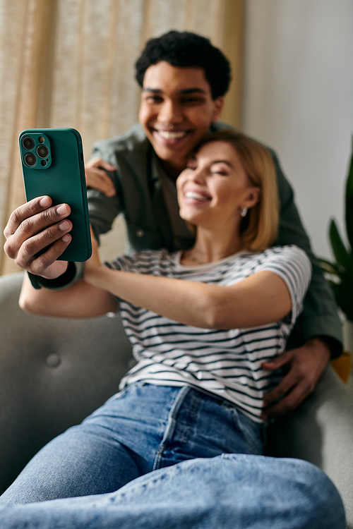 A young interracial couple smiles and takes a selfie together in their modern apartment.