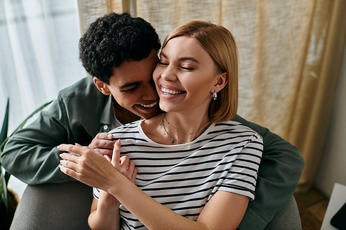 A young, multicultural couple enjoys a moment of intimacy and laughter in their modern apartment.