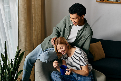 A young couple enjoys a cozy moment in their modern apartment, laughing and sharing a cup of coffee.