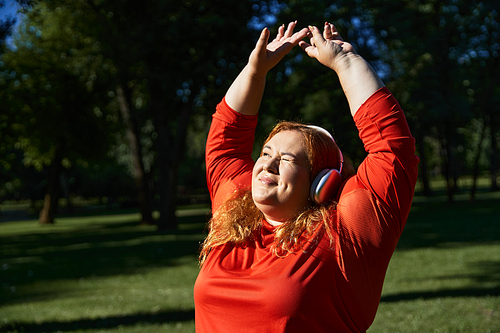 Plus size woman embraces fitness with a stretch in the sunny park.