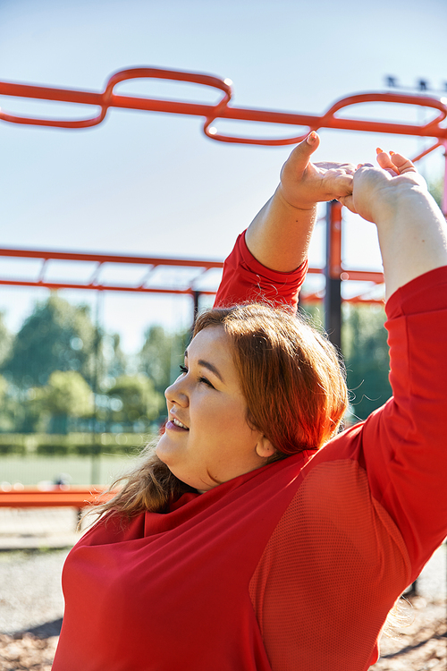 A cheerful woman stretches under the vibrant blue sky in the park.