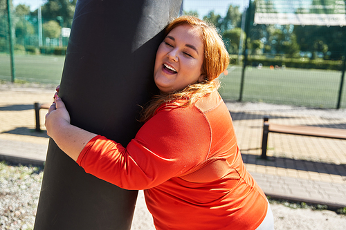 A joyful woman embraces a fitness pole while exercising in the park.