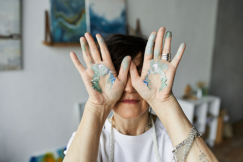 A woman playfully displays her paint stained hands while enjoying her artistic process.