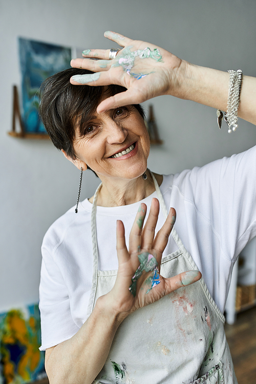 A happy woman with paint covered hands enjoys her artistic process.