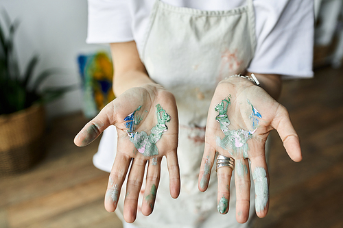 A mature artist with paint splattered hands blends colors happily in her studio.