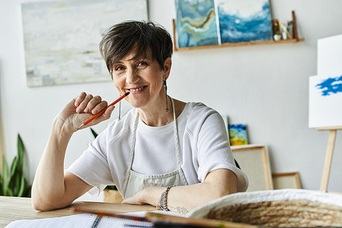 A painter smiles thoughtfully while taking a break in her vibrant art studio.