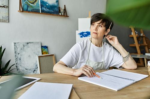 A woman thoughtfully sketches in her vibrant art studio.