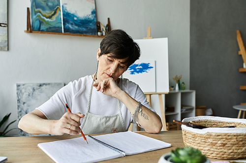 A dedicated artist sketches thoughtfully at her studio table.