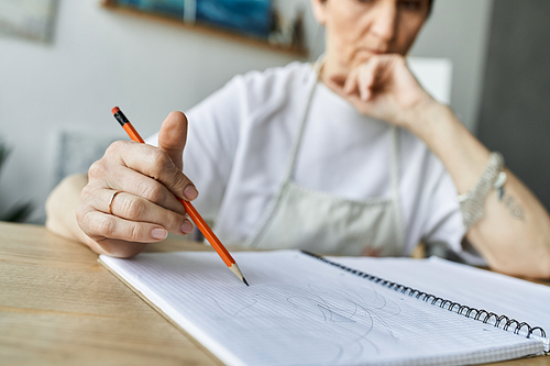 A mature woman concentrates as she sketches in her cozy art studio.