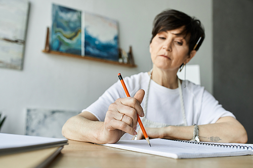 A woman thoughtfully sketches in her colorful art studio.