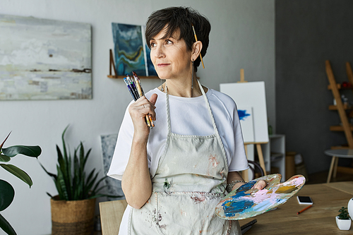 A mature woman ponders her next brushstroke amidst colorful creations.