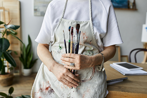 A skilled painter joyfully embraces her tools in a bright art studio.