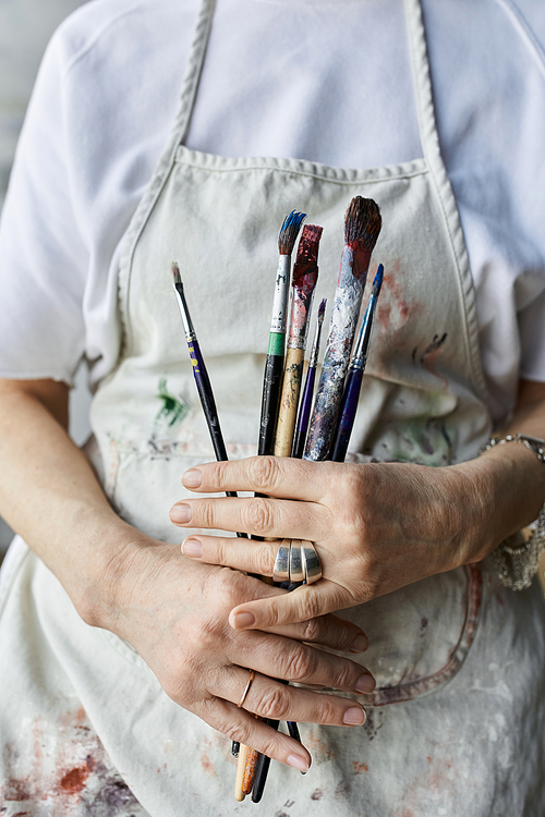 A woman in an art studio holds her paintbrushes while immersed in creativity.