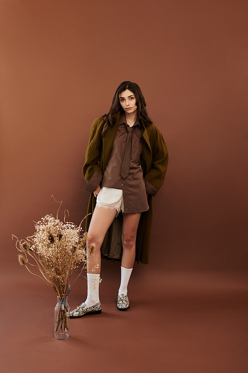 A young woman poses confidently in a fashionable autumn outfit against a warm backdrop, embodying seasonal style.