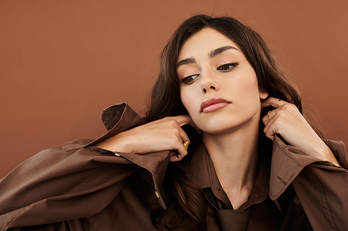 A young woman poses gracefully, highlighting her autumn fashion against a warm studio backdrop, embodying seasonal elegance.