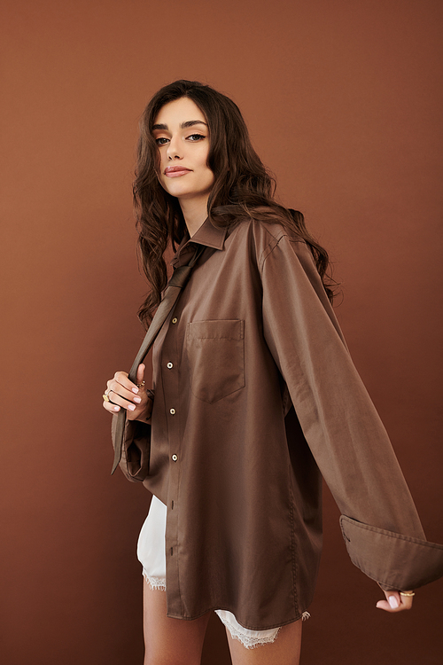 A young woman confidently poses in a chic autumn outfit, beautifully styled in a warm, earthy-toned studio space.