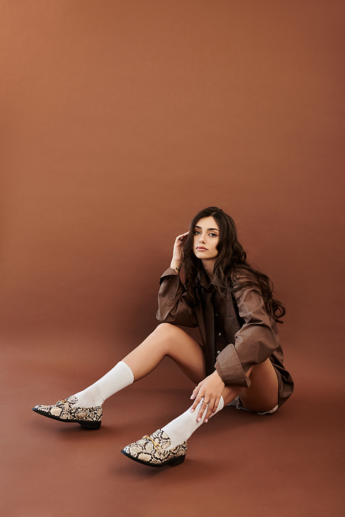 A young woman radiates confidence while posing in a trendy autumn outfit against a rich, warm backdrop, capturing seasonal style.