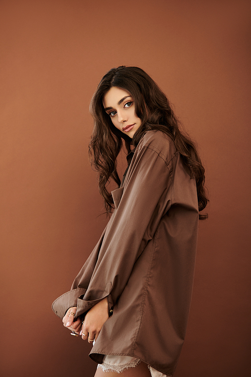 A beautiful young woman poses effortlessly in a chic autumn outfit, embodying warmth and elegance in a cozy studio atmosphere.