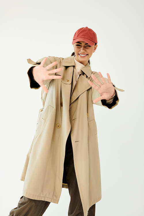 A young woman playfully poses in a chic autumn outfit, radiating joy and style in a minimalistic studio.