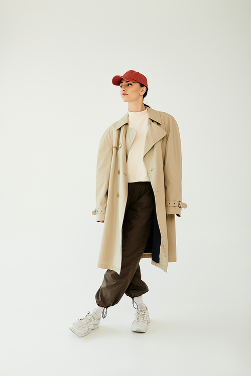 A fashionable young woman showcases a chic autumn outfit, exuding confidence in a studio with minimalist style.