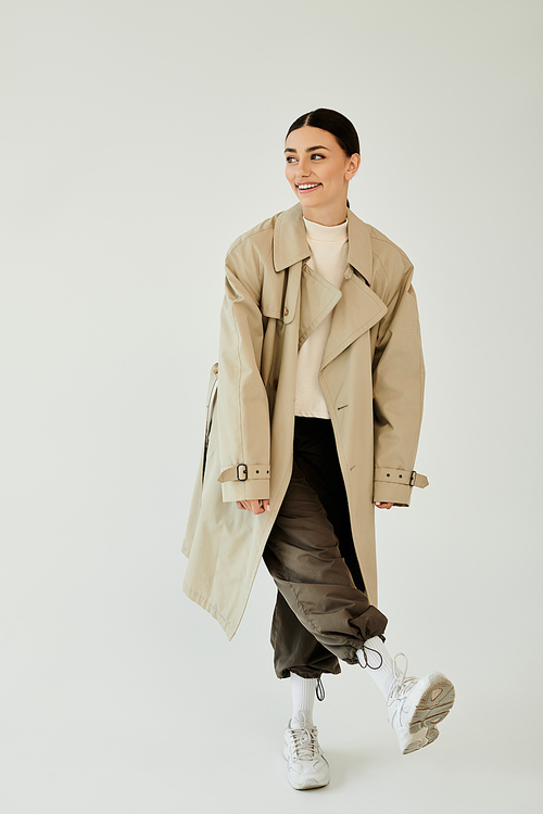 A young woman is elegantly posing in a trendy autumn outfit, radiating confidence in a serene studio backdrop.