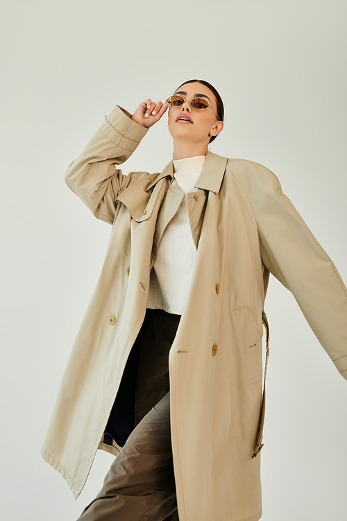 A young woman elegantly poses in a trendy autumn outfit, embodying seasonal elegance amidst a clean studio backdrop.