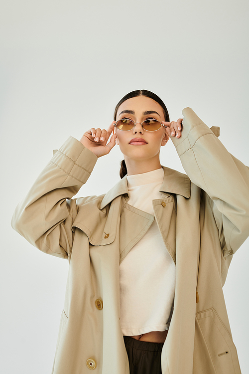 A young woman elegantly poses in an autumnal outfit, highlighting the season's style in a minimalist studio ambiance.