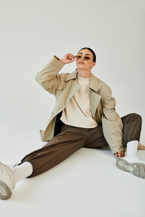 A young woman dons a chic autumn ensemble, exuding confidence while posing stylishly in a minimalist studio.